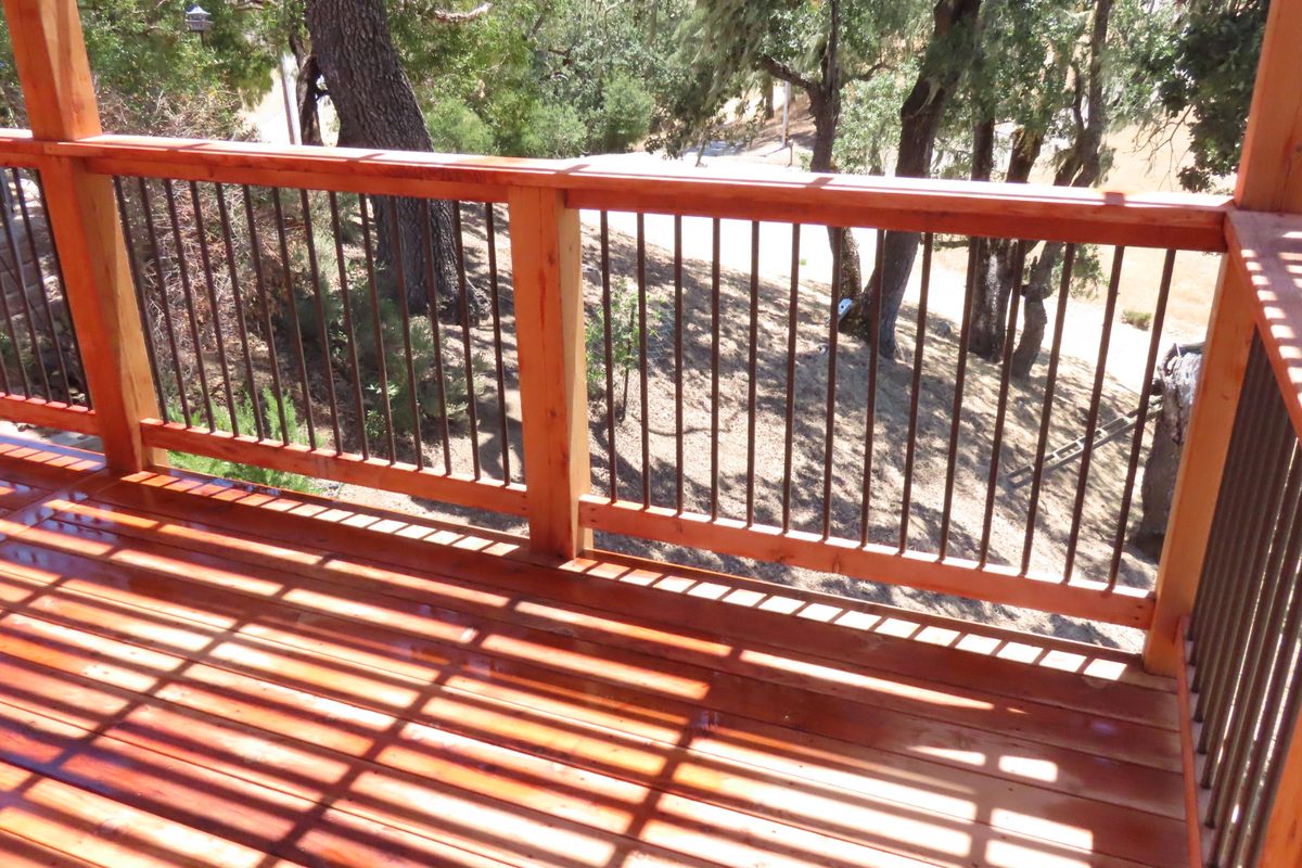 A stained deck railing with wood posts and metal balusters, trees beyond.