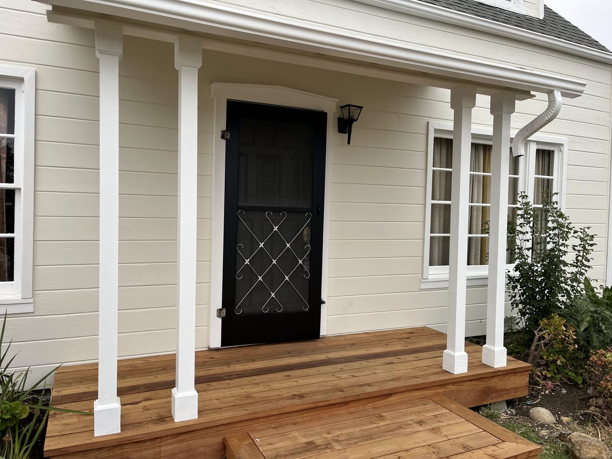 A new wood porch and step in front of a white house with white columns and a black front door.
